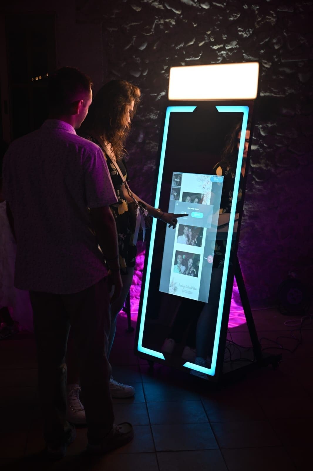 Invités interagissant avec l'écran tactile du photobooth miroir pendant la soirée de mariage