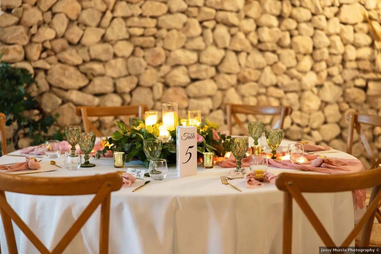 Table de mariage ronde avec bougies, verres verts et mur de pierre en Provence